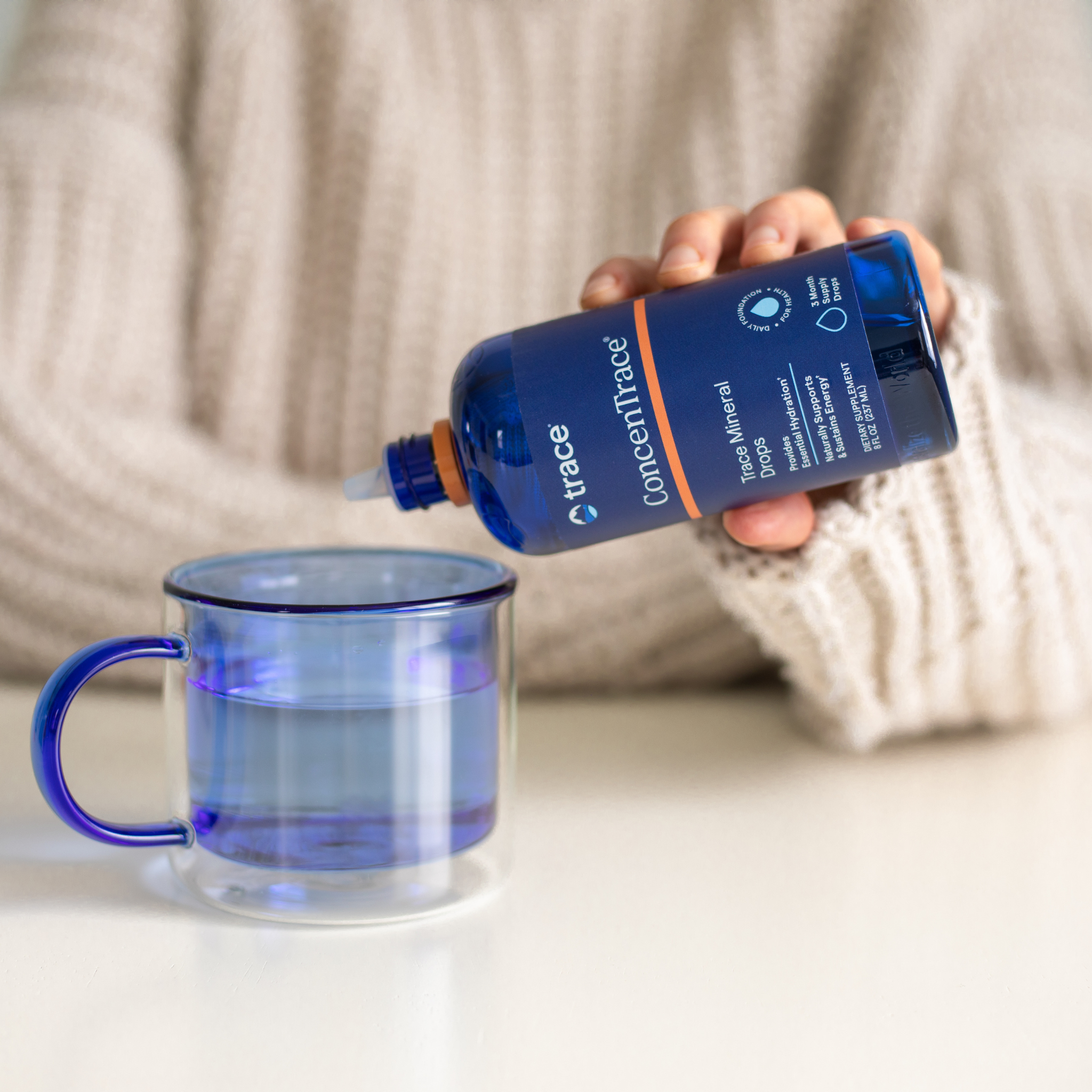 Trace minerals Concentrace joninių mineralų pakuotė, kurią laiko moteris paverstą ir lašina į vandens stiklinę