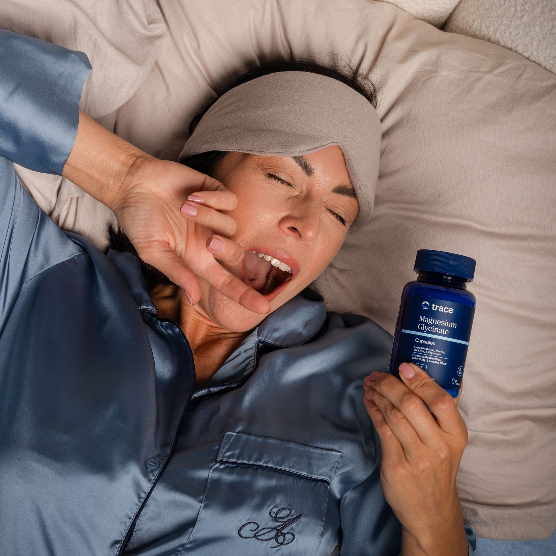 Moteris guli lovoje, žiovauja ir laiko magnio glicinato maisto papildą.